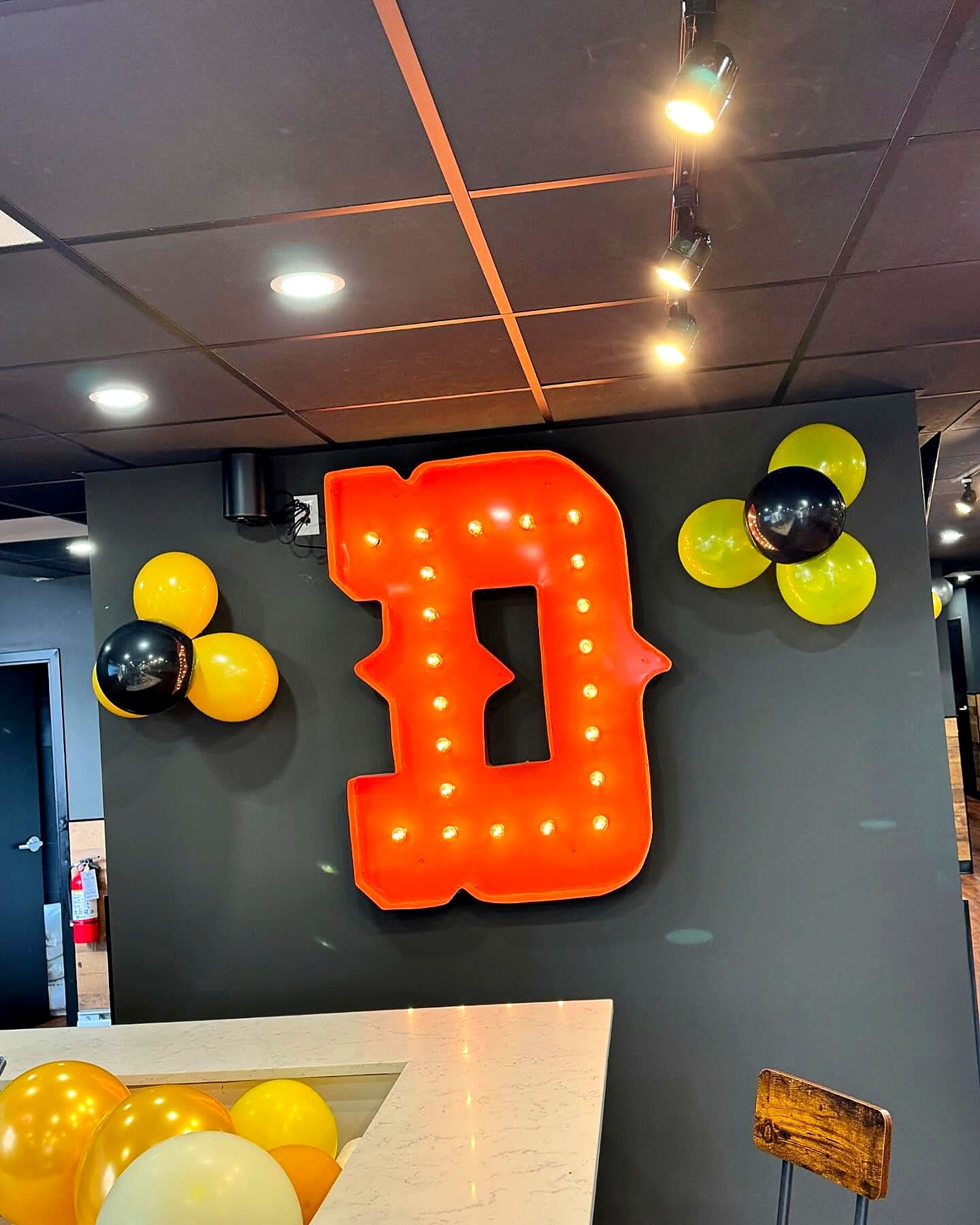 Orange marquee-style letter D with bulbs on the wall inside Dickey's Barbecue Pit